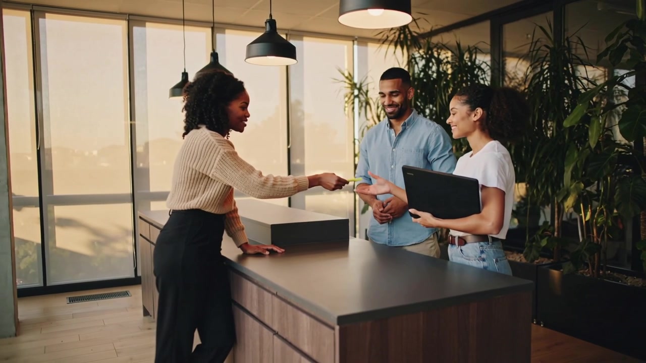 Extending receptionist in beige sweater passing key at lobby, visitors accepting laptop for access