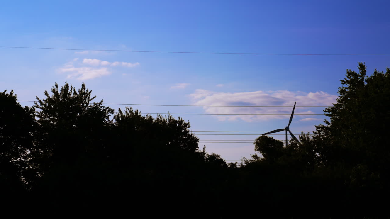 Turbine silhouette at dusk. A wind turbine stands tall amidst trees, creating a serene silhouette under the fading light of dusk
