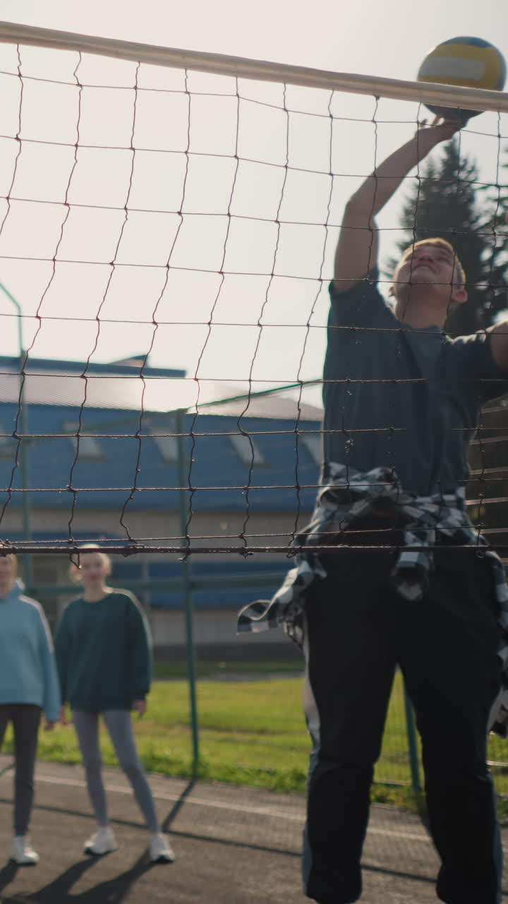 배경에서 건물이 보이는 야외 배구 경기장, 배경에서 주의 깊게 지켜보는 두 명의 여성과 함께 배구 훈련 초보자