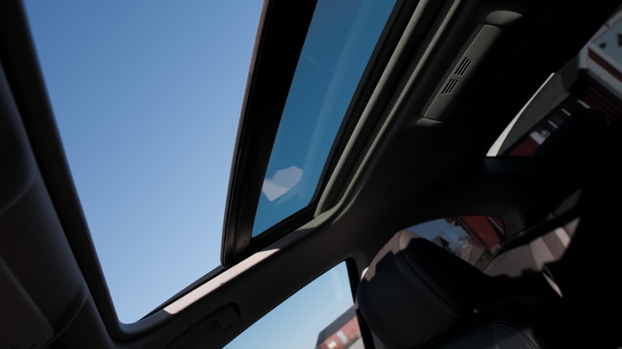 Mani scandinave che aprono un tettuccio apribile in vetro, rivelando un cielo azzurro e nuvoloso, lasciando uscire l'aria calda e facendo entrare una brezza rinfrescante durante un viaggio in auto, per prendere una boccata d'aria fresca in una calda e afosa estate del 2021