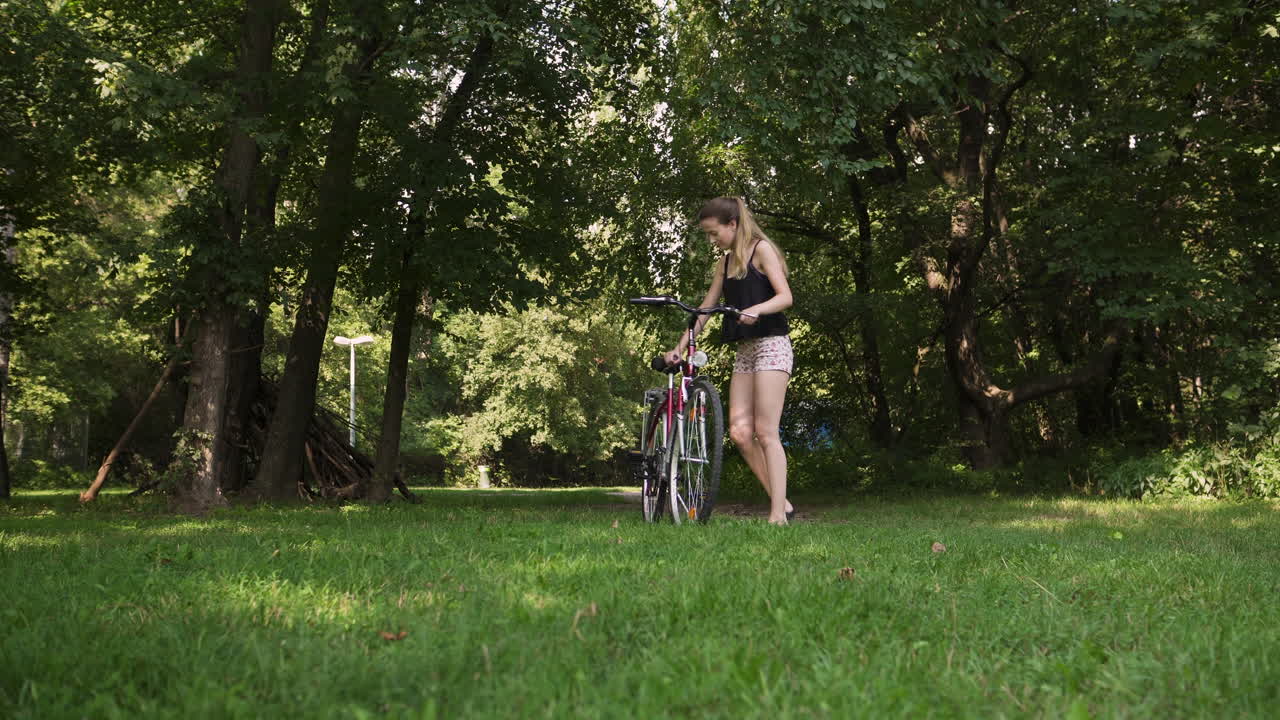 예쁜 여자가 풀이 무성한 공원 지역에 자전거를 주차합니다.