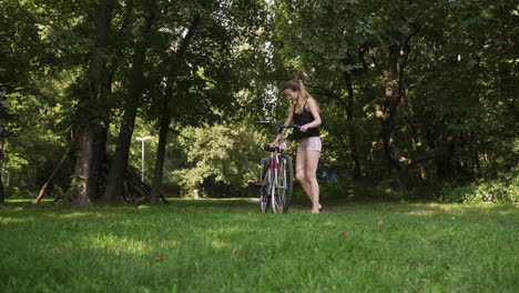 una mujer bonita aparca su bicicleta en un parque cubierto de hierba