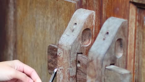 close-up of hands using a key to unlock an antique wooden door mechanism.