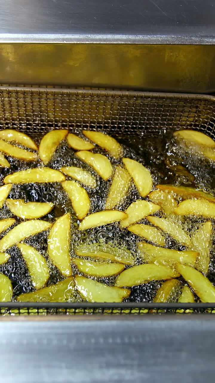 Potato in deep fryer. Crispy fries in the deep fryer in a fast food restaurant. Cooking potato. Junk food concept. Top view. Close up. Vertical video