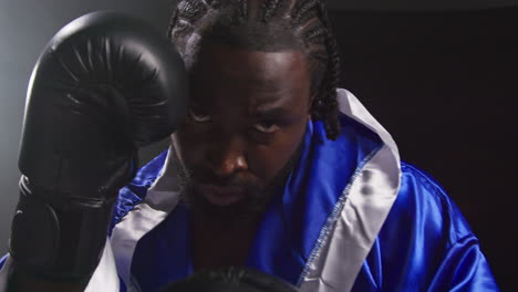 portrait of boxer wearing robe in ring at start of boxing match putting up boxing gloves ready to fight