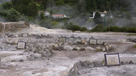 manantial volcánico natural caliente con vapor que se eleva y casas en el fondo