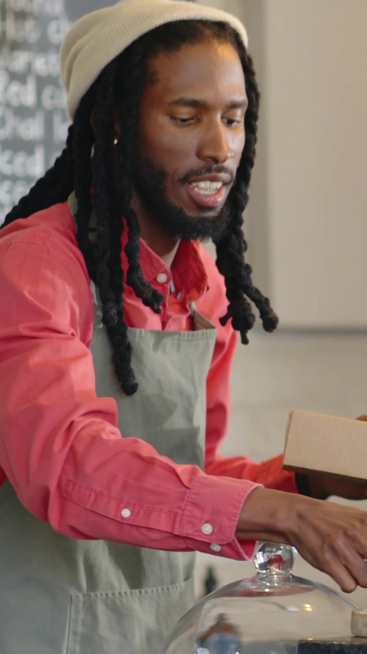 Vertical video: Holding open box, baker in apron placing cupcake with green tool at till for pickup