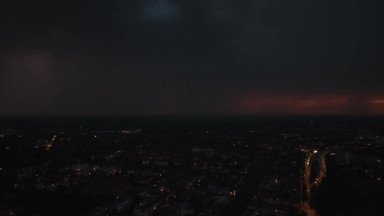 Blesky šlehající nad městem v noci, osvětlující mraky a panorama s auty jedoucími po ulici během bouřky. Fantastický letecký pohled z dronu s rotací a panoramatickým posunem doprava.