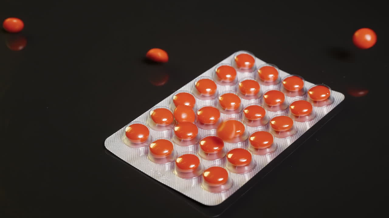 Capsule, pillole e compresse di vitamine rosse che cadono su un blister scontrandosi, suggerendo temi farmaceutici e di medicazione, concetti di trattamento medico e salute ideali per illustrare il benessere sanitario.