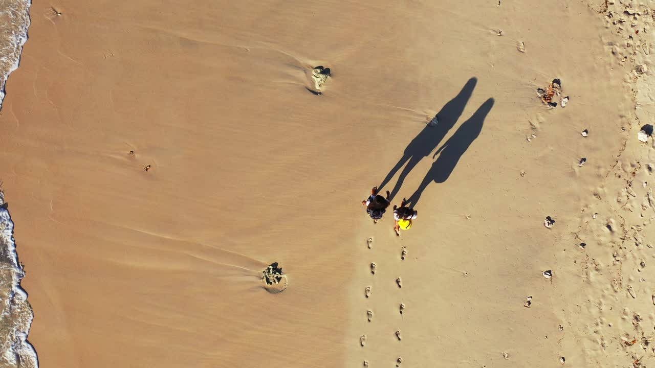 Two girls walking on golden sandy beach with waves splashing the coast on sunny day in Hawaii
