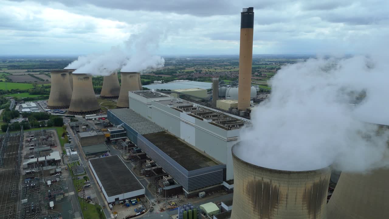 Tracking drone shot along access roads to a major power station with cooling towers and industrial yard in UK