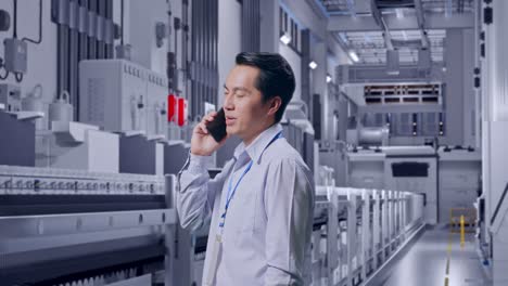 side view asian male professional worker standing at pharmaceutical factory, vaccine production facility, he pick the phone up and started to specking to it with a slicely smile