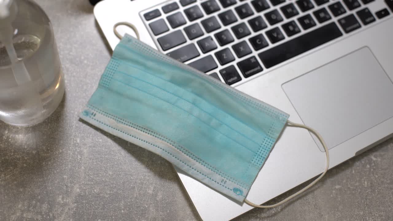 computadora portátil con máscara facial médica, bloc de notas y lápiz en la parte superior junto con una taza de café en la mesa de comedor. configuración en el hogar. concepto de trabajo en el hogar.