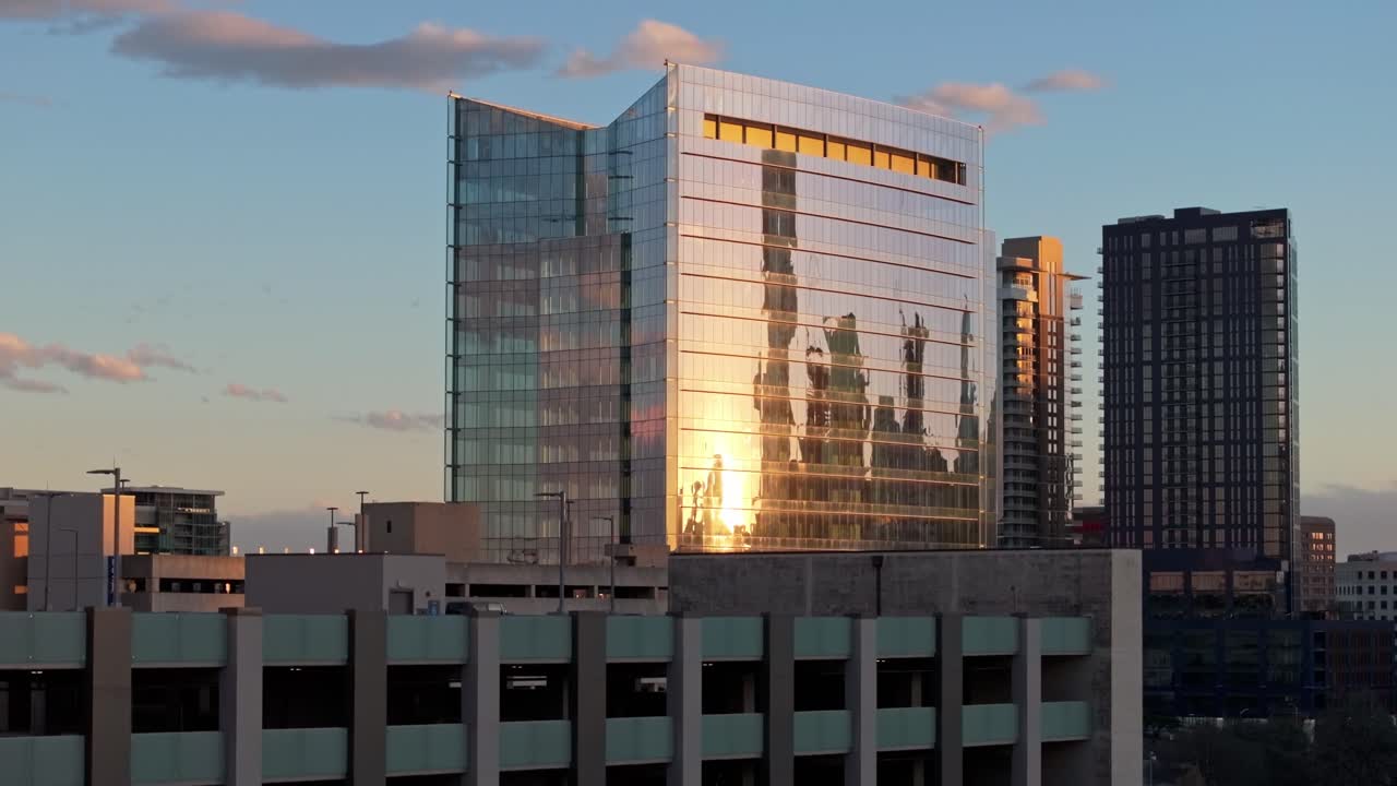 A zoomed in drone shot with parallax decreasing elevation and centered on a parking garage and a building near the University Medical Center in Austin Texas with sunset reflecting off the windows