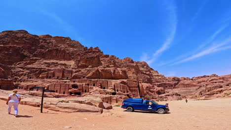 people rest in the shade of the tree in petra, jordan, west asia. low angle panoramic view on the street of facades at the backdrop of blue sky.