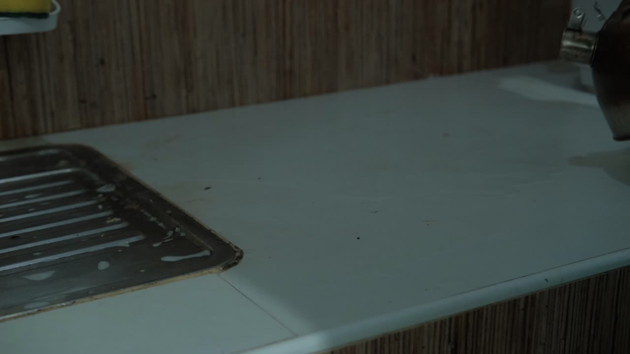 Medium static shot of person pouring hot water from kettle on kitchen countertop to disinfect.