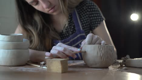 primer plano de la mano de una mujer joven haciendo cerámica y cerámica en un taller, trabajando con arcilla. crear un patrón en el producto.