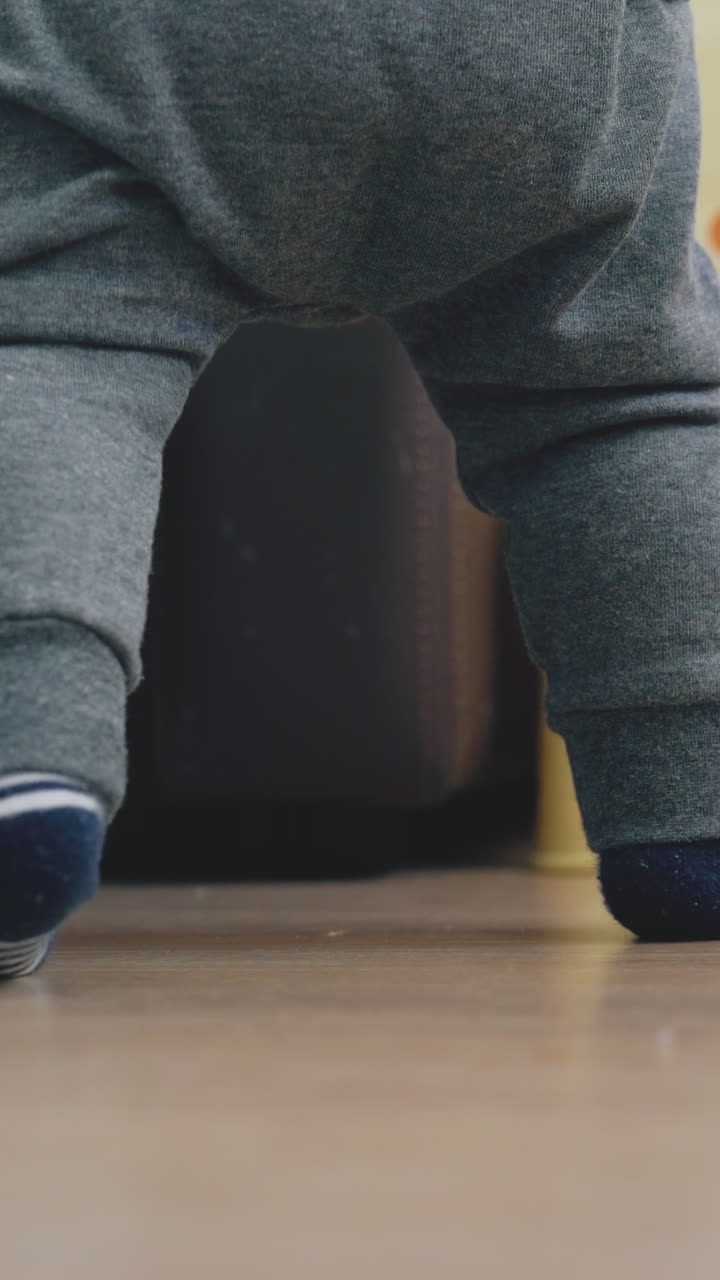 playful baby in grey pants plays with nozzle suction at large bed on wooden floor in children room close low angle shot