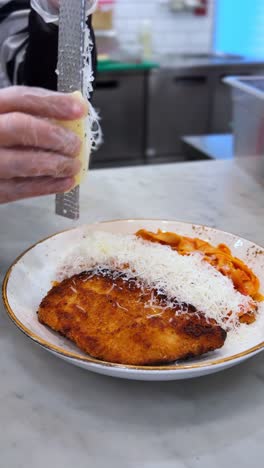 close-up of crispy chicken parmesan topped with freshly grated cheese over red sauce pasta. captured in vertical 4k, perfect for food promos and restaurant content.