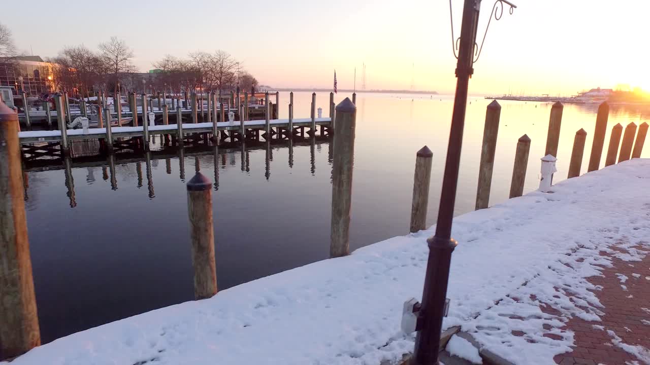 una toma aérea de bajo vuelo sobre un muelle cubierto de nieve en annapolis, maryland, durante el amanecer púrpura y dorado
