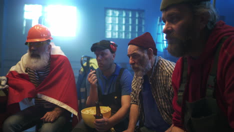 group of blue-collar men watching a game with beer and chips