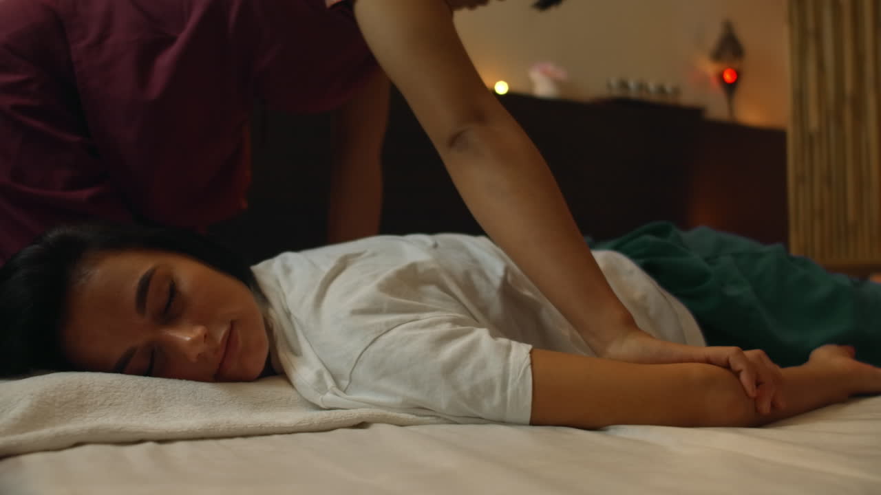 Asian Woman performs Traditional Thai Massage to beautiful European Woman. Rehabilitation and Treatment after Injuries with the help of Massage. Relax and Rest from massage of Legs Arms and Back. Therapeutic massage