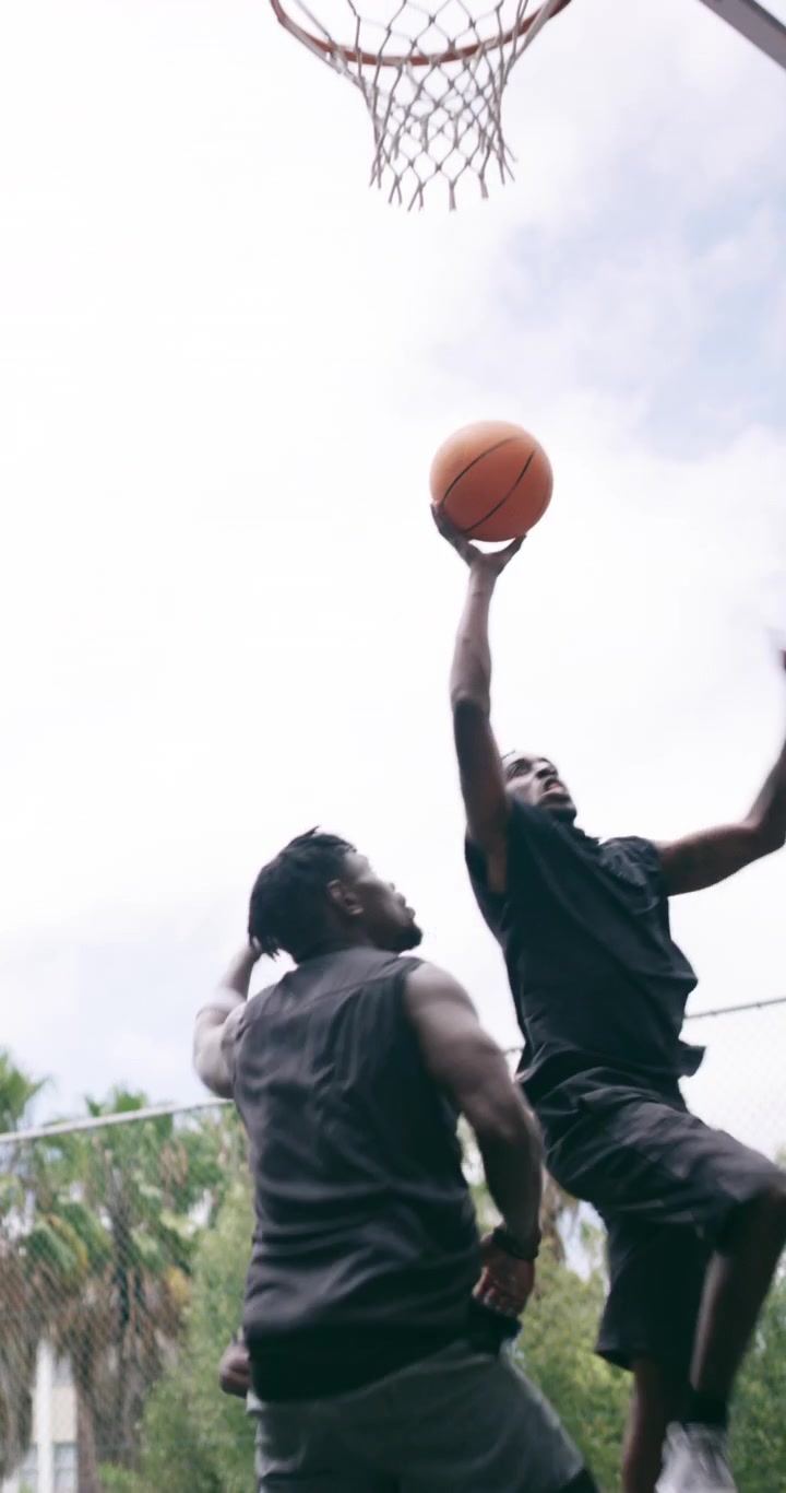 Giovani uomini che giocano a basket su un campo all'aperto.