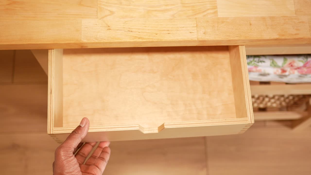 A person's hand opening an empty wooden drawer