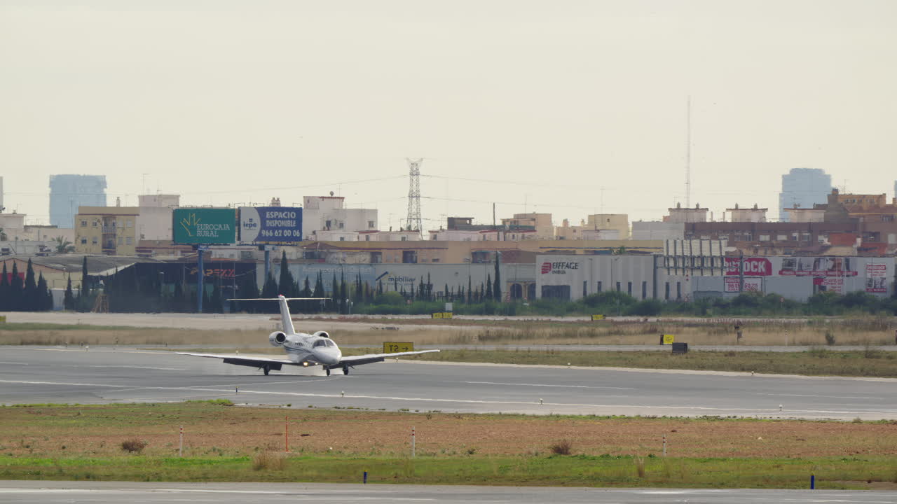 Atterraggio e rullaggio di jet privato su pista aeroportuale con sfondo urbano