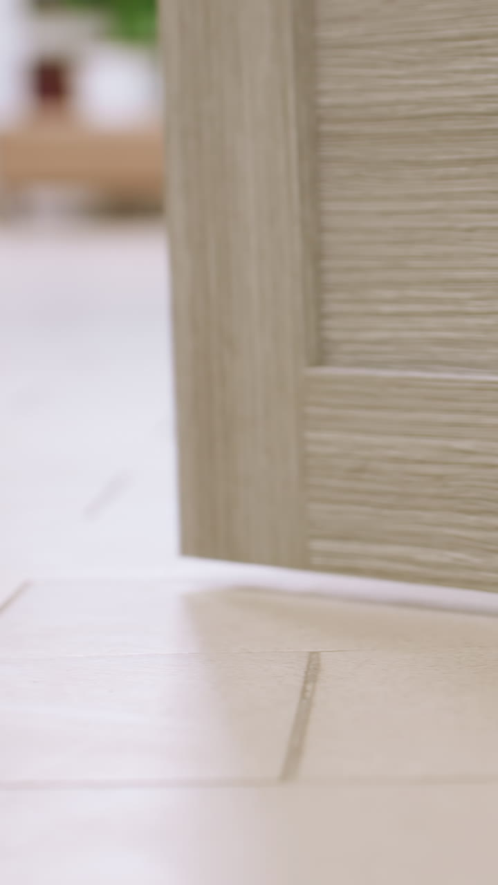caucasian therapist feet approach wooden door threshold in clinic, white clogs on tiled floor, closeup of sole crossing gap under door, subtle hinge and frame detail, quiet corridor entry