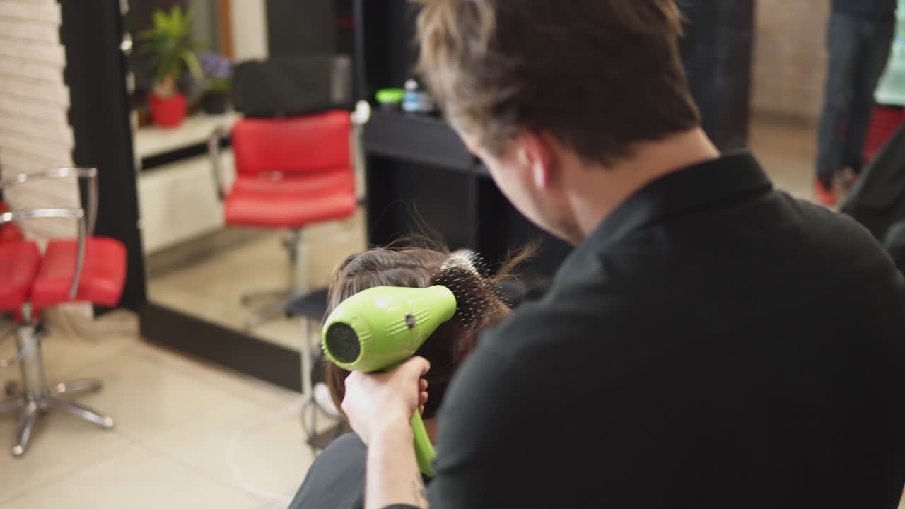 Professional hairdresser is drying hair of young attractive woman in beauty salon. Shot in 4k