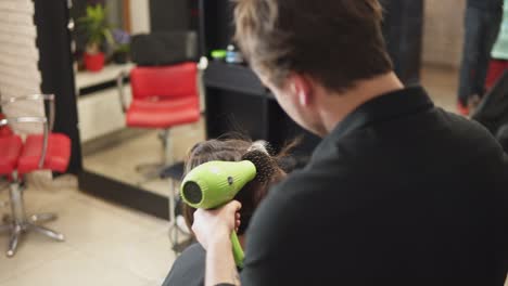un peluquero profesional está secando el cabello de una mujer joven y atractiva en un salón de belleza. filmado en 4k