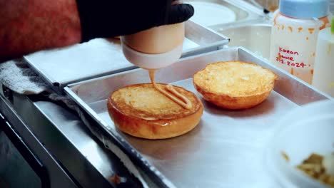 imágenes cinematográficas de cocina de 4k de un chef preparando y haciendo una deliciosa hamburguesa casera en la cocina de un restaurante en cámara lenta poniendo salsa en los panes