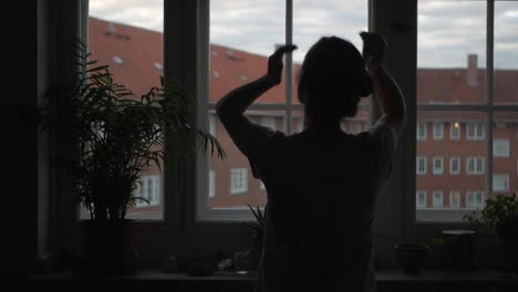 Woman-standing-in-front-of-apartment-window-in-morning-and-touches-hair