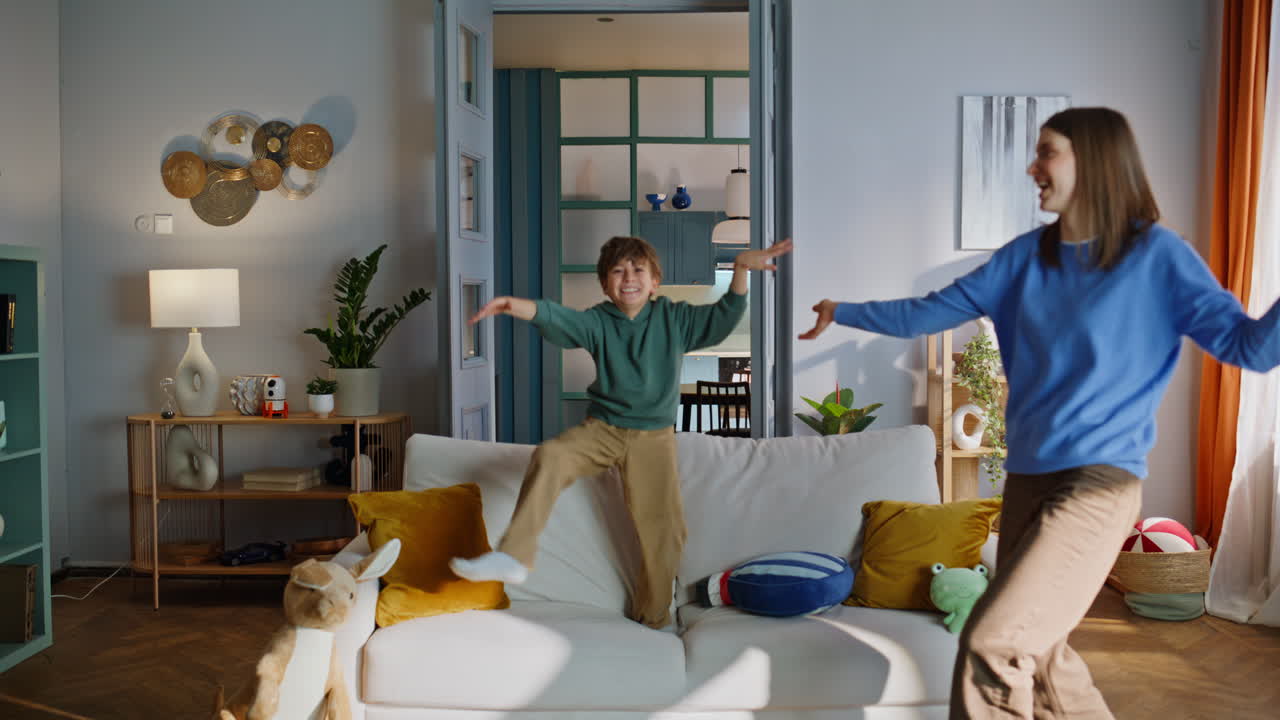 Playful mother son dancing having fun in home living room. Funny boy jumping