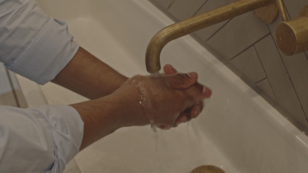 Handheld shot of dark skinned man washing his hands and turning off faucet