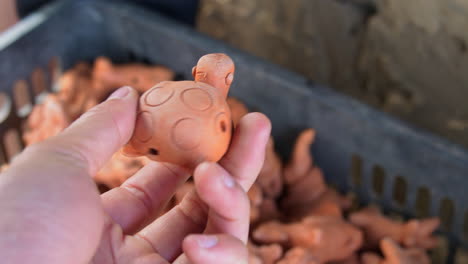 Close up view of hand holding traditional clay figurine of turtle in southeast asian pottery style