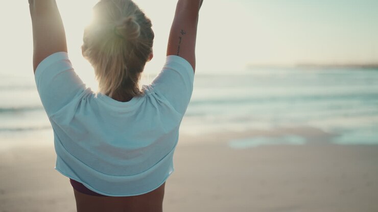 Vista trasera de mujer en forma levantando los brazos y haciendo yoga en la playa