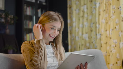 Mujer-Joven-Feliz-Con-Auriculares-Viendo-Videos-Divertidos-En-La-Tableta-Mientras-Se-Sienta-En-El-Sofá-En-Casa