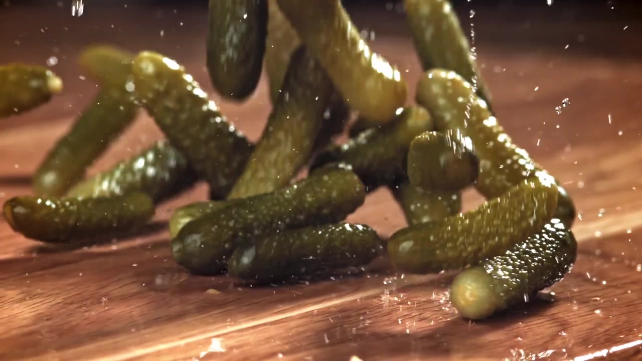 Cornichons tombant et éclaboussant sur une surface en bois mouillée au ralenti