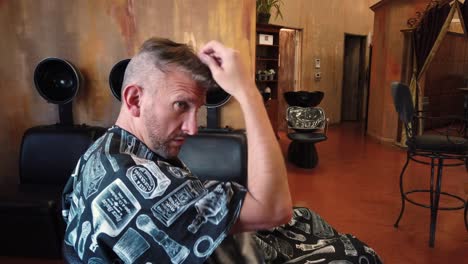 hombre pasando los dedos por el cabello, peinando el cabello después de que el peluquero acaba de cortar
