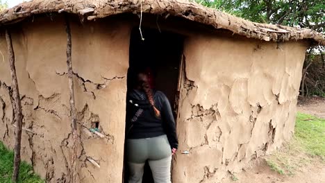 woman entering into a local maasai rural handmade mud house with a masai person