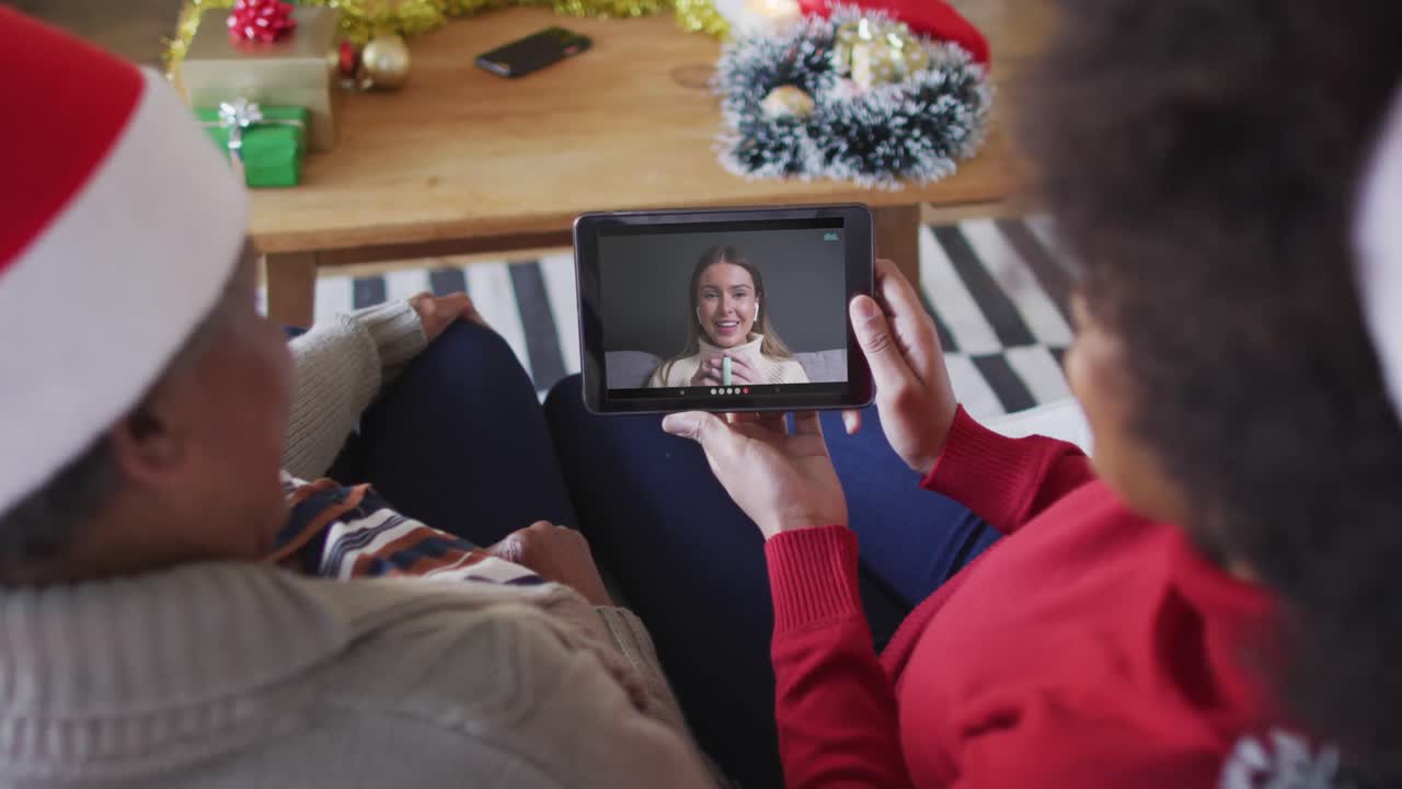 madre y hija afroamericanas usando una tableta para una videollamada de navidad con una mujer en la pantalla