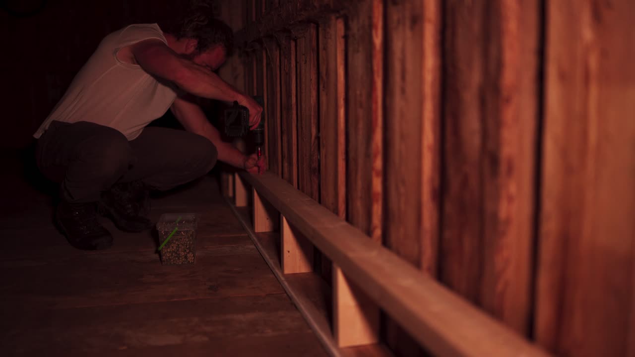 백인 남자가 창고 안에서 전기 스크루드라이버를 사용하여 목공 일을 하고 있습니다.