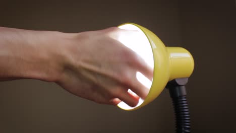 close up of a hand putting a light bulb on a yellow lamp