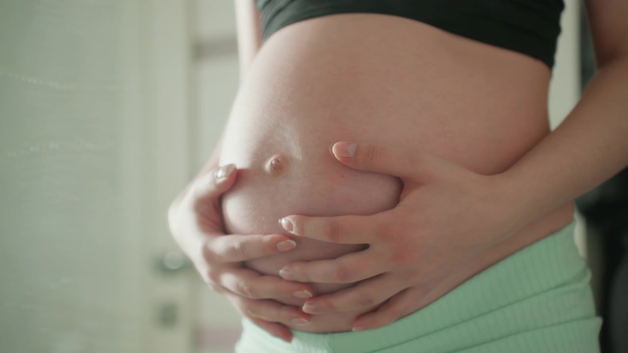 Manos de mujer embarazada acariciando tiernamente su barriga.