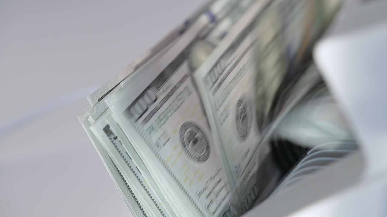 One hundred dollar banknotes falling quickly on the holder of cash machine. US currency counted in the special equipment. Close up.