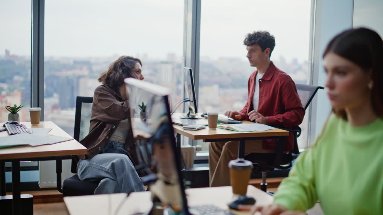 Startup team, der arbejder sammen ved skriveborde og deler idéer i et lyst kontor med åbne kontorlandskaber