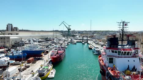 Aerial-drone-shot-rising-over-blue-seas-revealing-many-boats-and-ships-in-a-very-busy-boat-yard