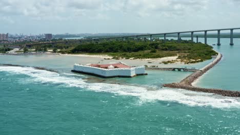 rotating aerial drone wide shot of the historic star shaped reis magos fort built on a reef with the large newton navarro bridge behind in the beach capital city of natal in rio grande do norte brazil